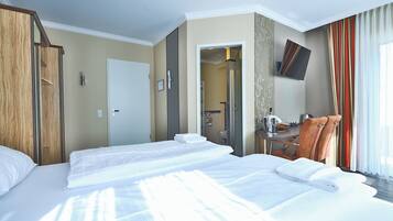 Habitación de hotel con dos camas, un escritorio, una silla, un televisor y un baño visible a través de una puerta abierta.