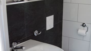 A bathroom with a white sink, toilet, and dark tiled walls.