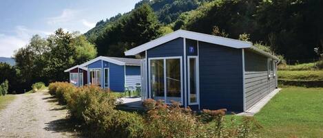 Une rangée de cabanes bleues, avec un chemin de gravier menant à elles, entourées de verdure et de collines.