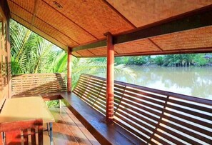 A covered outdoor area with a wooden bench and table, overlooking a calm river with lush greenery. - RuenNamyen Resort (Samut Songkhram)