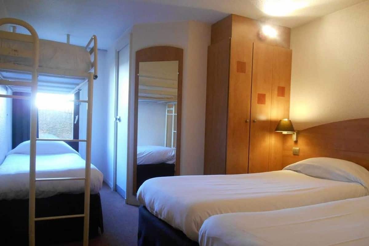 A dorm-style room with bunk beds, a wardrobe, and a bedside lamp.