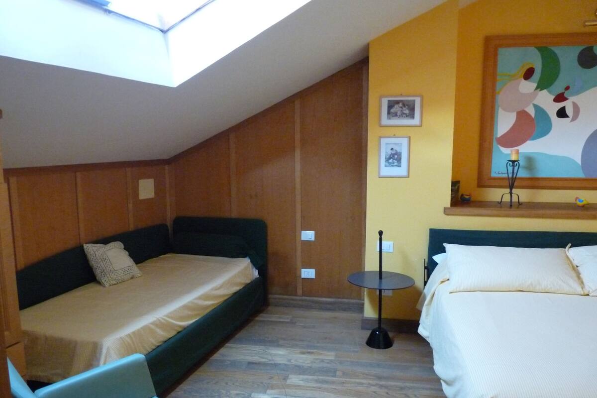 Ein Zimmer mit schräge Decke, zwei Betten mit weißen Laken, ein kleiner runder Tisch und ein Stuhl.