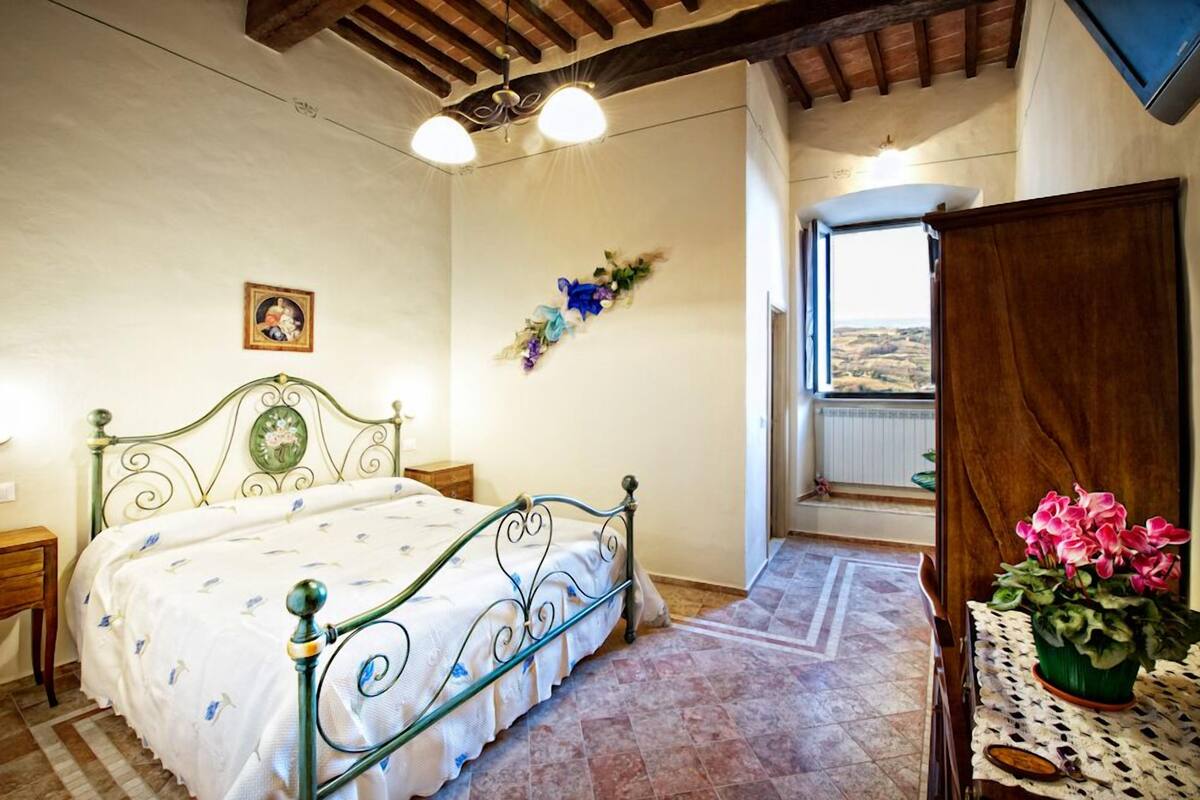 Ein Schlafzimmer mit Bett, Holz-Kopfteil, Nachttisch, Fenster mit Blick und einer Zimmerpflanze.