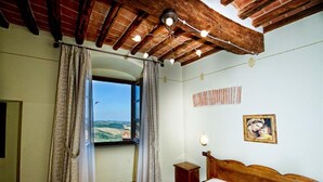 Une chambre avec un plafond en bois, un lit, une table de chevet, une fenêtre avec des rideaux et un tableau accroché au mur.
