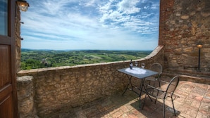 Un balcon aux murs de pierre, agrémenté d’une table et de chaises, qui offre une vue imprenable sur un paysage magnifique.