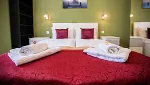 Habitación de hotel con dos camas, ropa de cama roja, cabeceros blancos y dos lámparas fijadas a la pared.