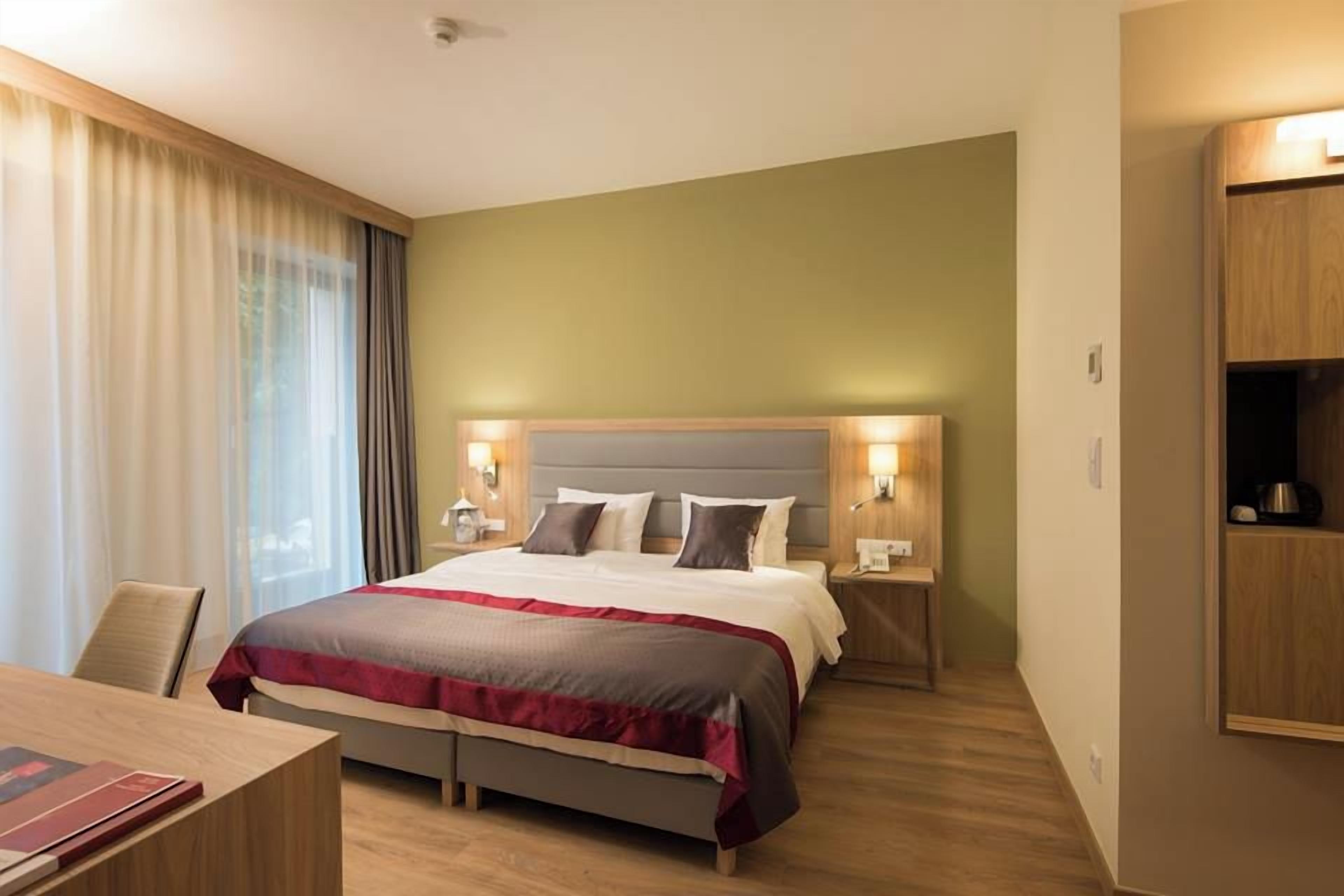 Habitació d'hotel amb llit, taules de nit, escriptori i armari.