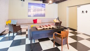 Un moderno vestíbulo de hotel con piso a cuadros, una zona de estar con sofá y sillones, una mesa con lámpara y un cuadro de paisaje urbano en la pared.