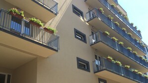 Un edificio de varios pisos con balcones decorados con plantas en macetas. La fachada es beige con marcos de ventanas oscuros.
