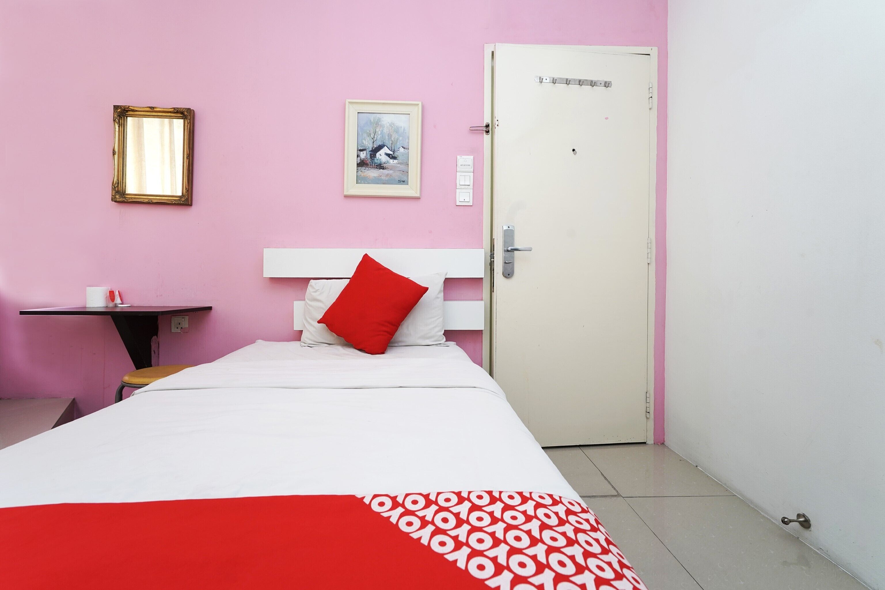 Una habitación con cama, una mesita, una silla, una puerta y un cuadro en la pared.