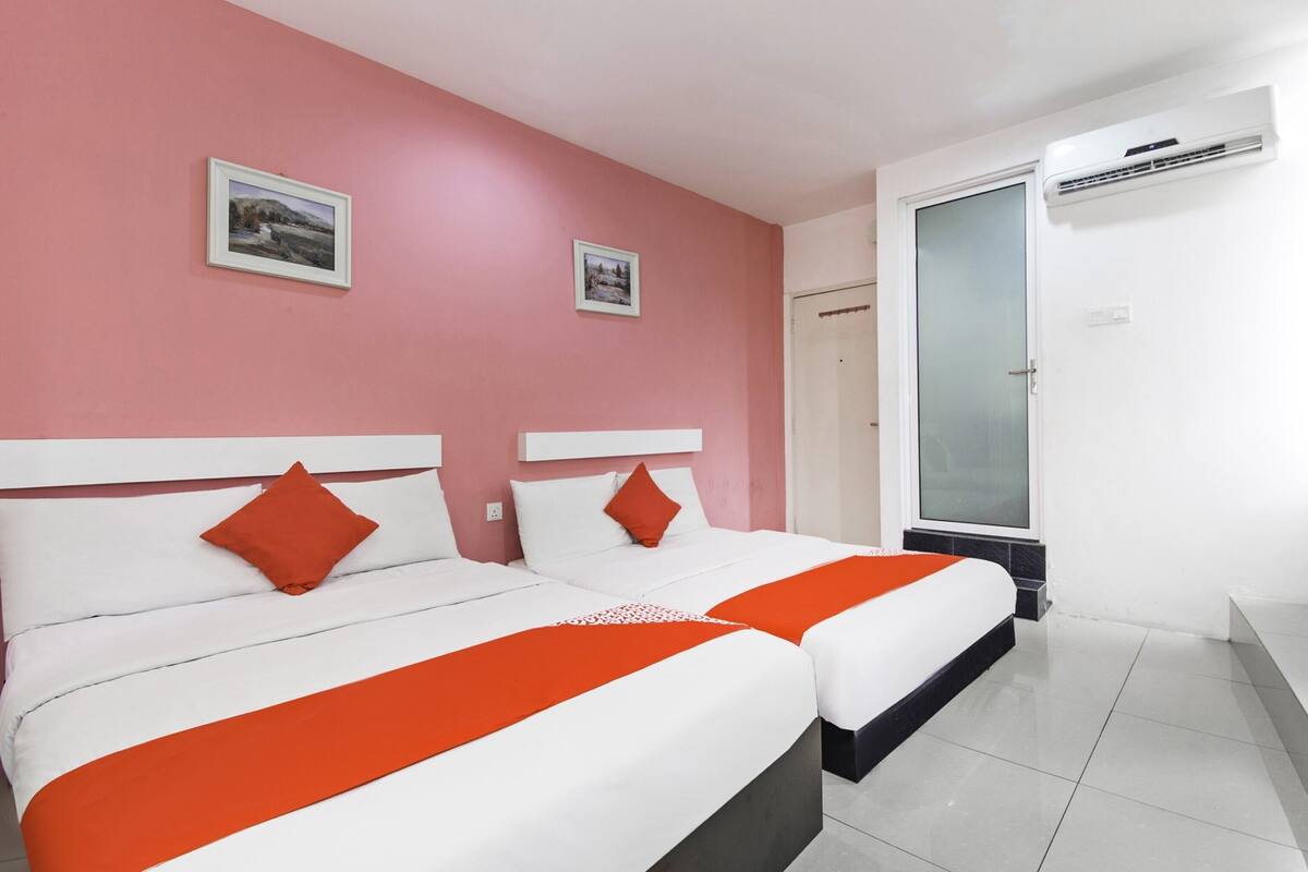 Hotellihuone, jossa on kaksi sänkyä, vaaleanpunaiset seinät ja kaksi kehystettyä kuvaa.