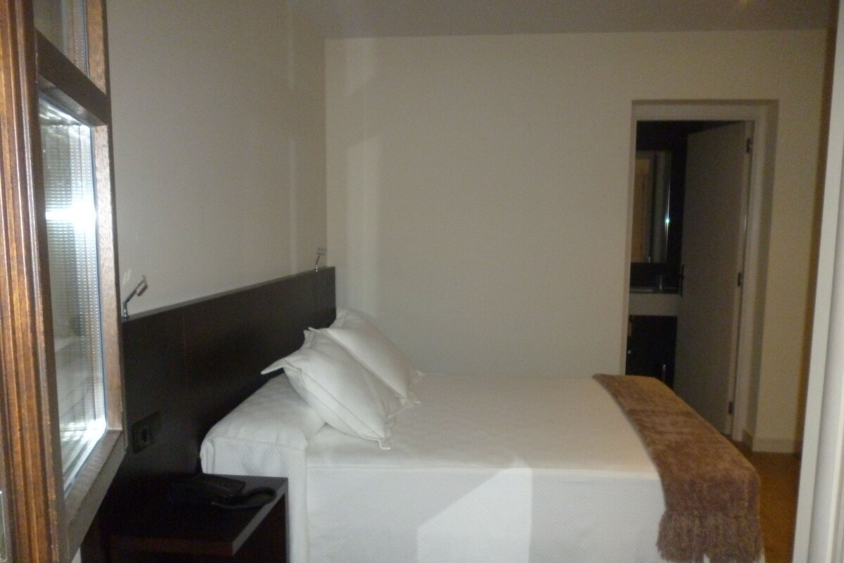 A hotel room with a bed, a nightstand, a mirror, and a door leading to another room.