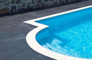 A swimming pool with a curved edge and a stone wall in the background. - Hotel Villa Marrón (Llanes)