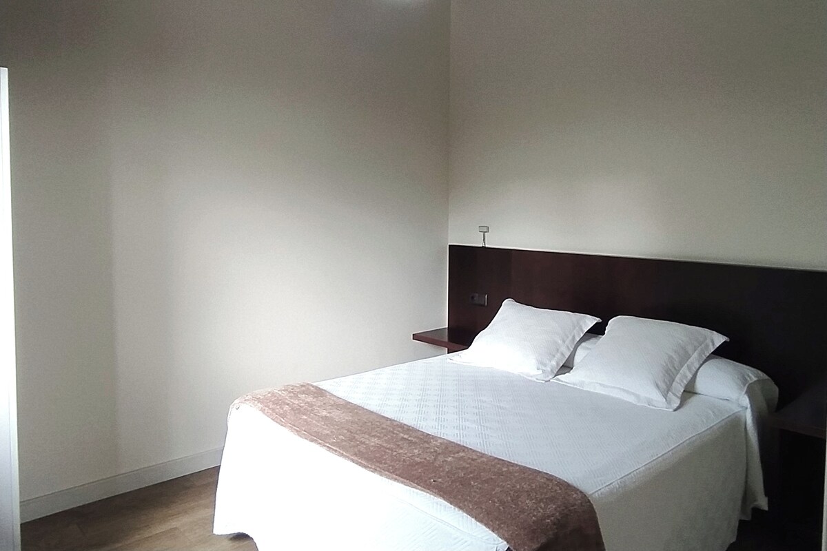 A bedroom with a bed, a nightstand, and a wall-mounted light fixture.