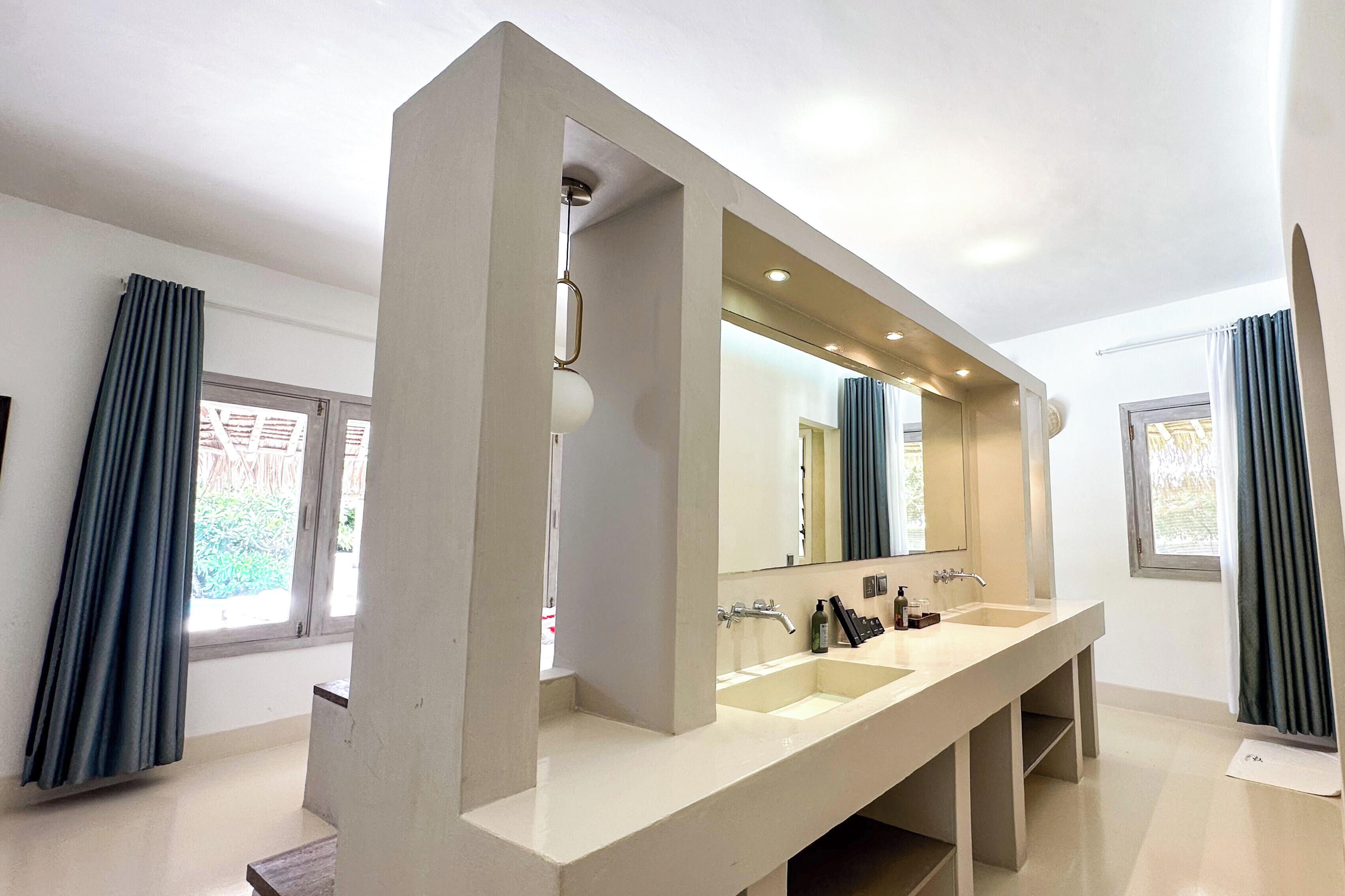 A modern bathroom with a large mirror, two sinks, and a shower area.