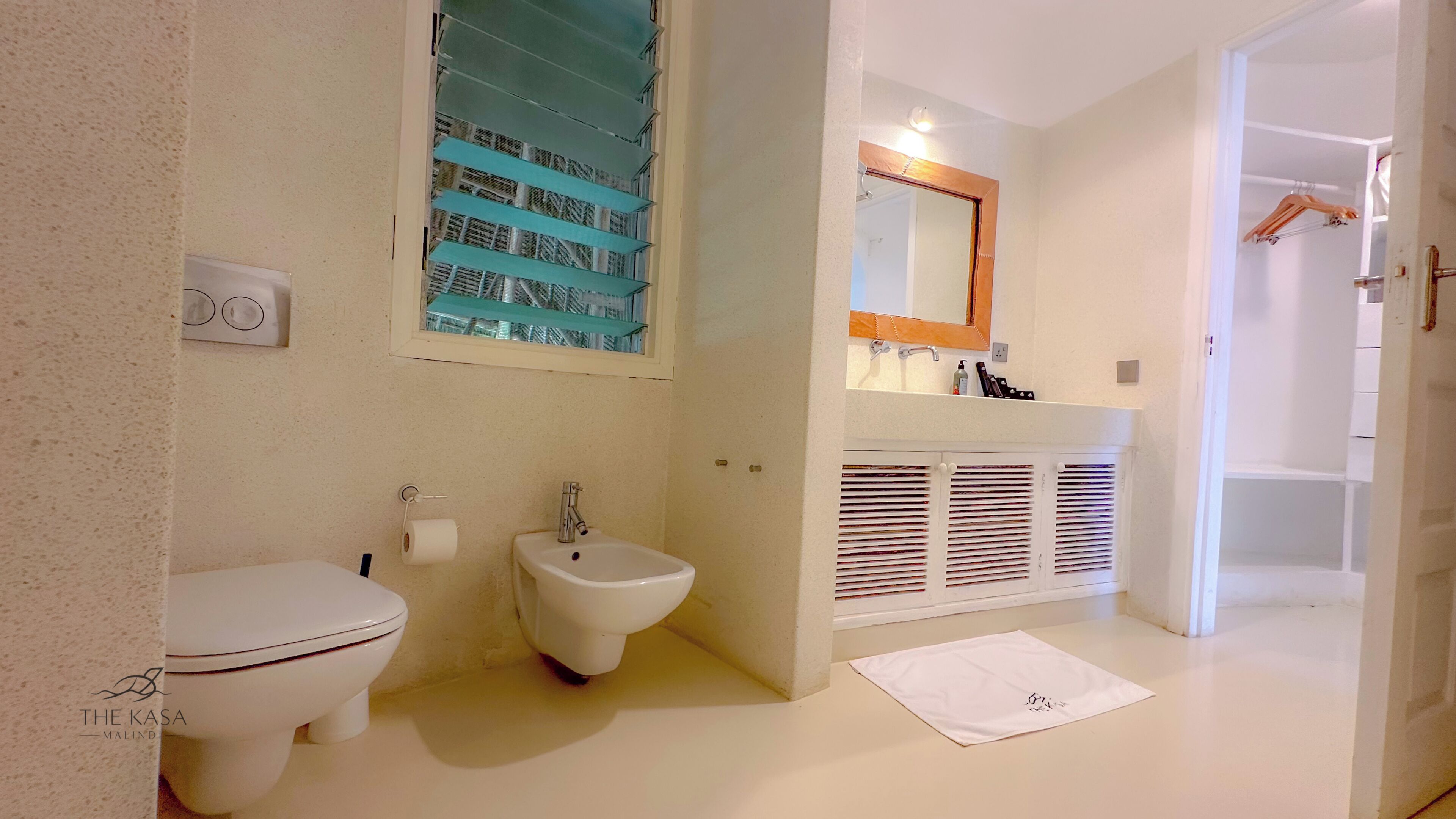 A bathroom with a toilet, bidet, sink, mirror, and a towel on the floor.