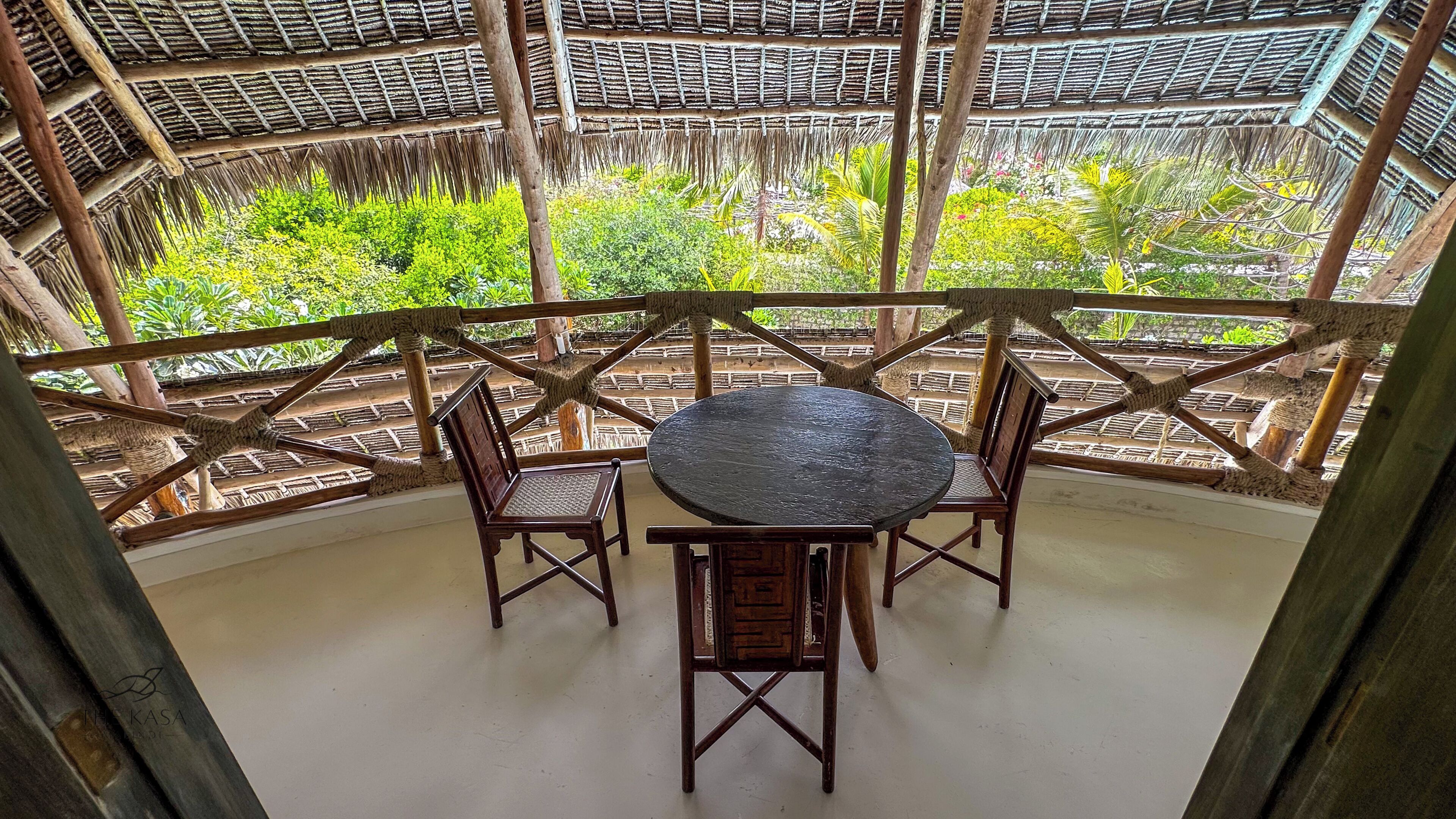 A covered outdoor seating area with a round table and four chairs, surrounded by a wooden lattice structure.