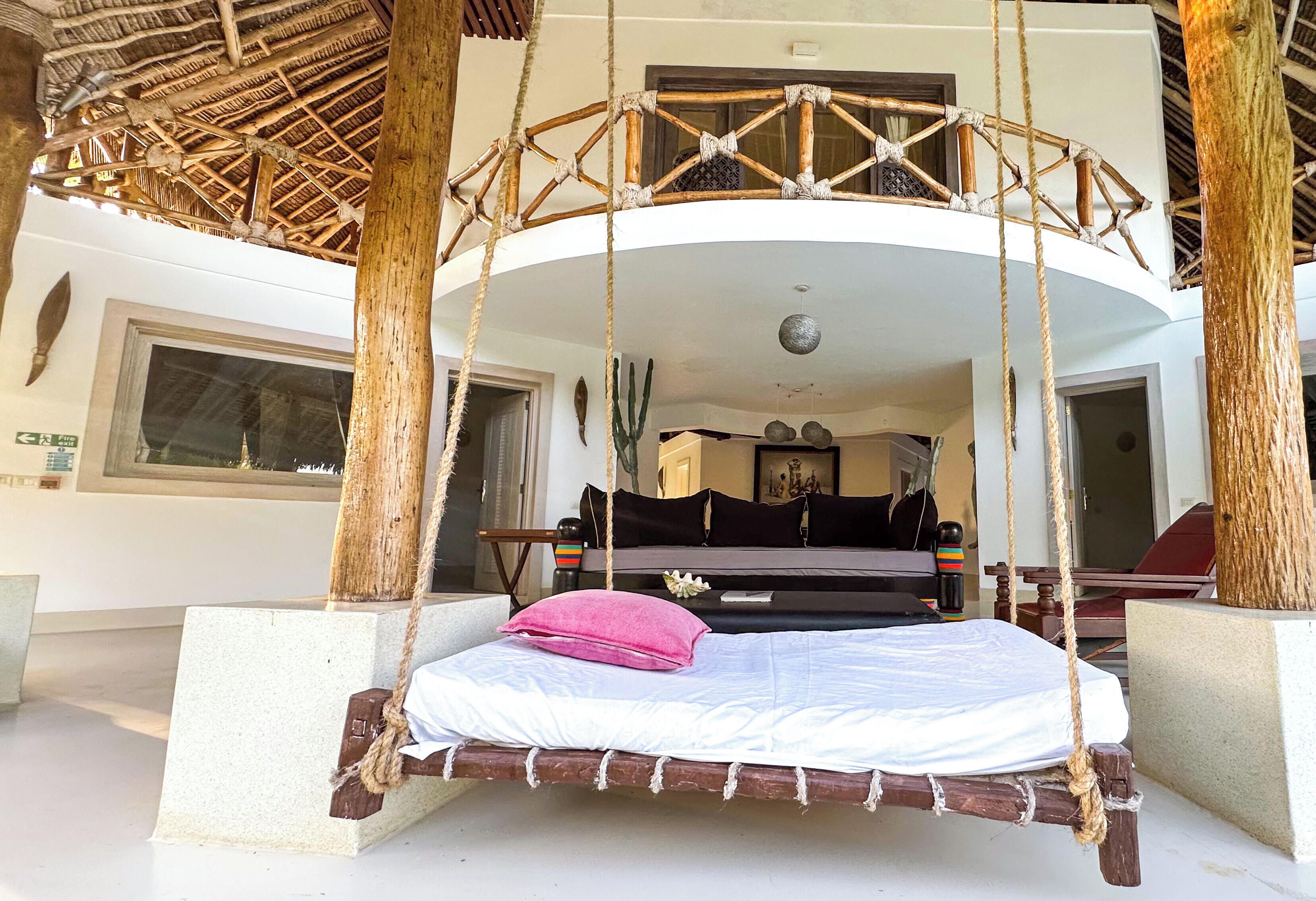 A room with a bed suspended from ropes, a window, and a door.
