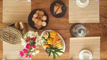 Una mesa de madera con diversos alimentos, entre ellos, un plato de galletas, un tazón de fruta y una cesta de pan.