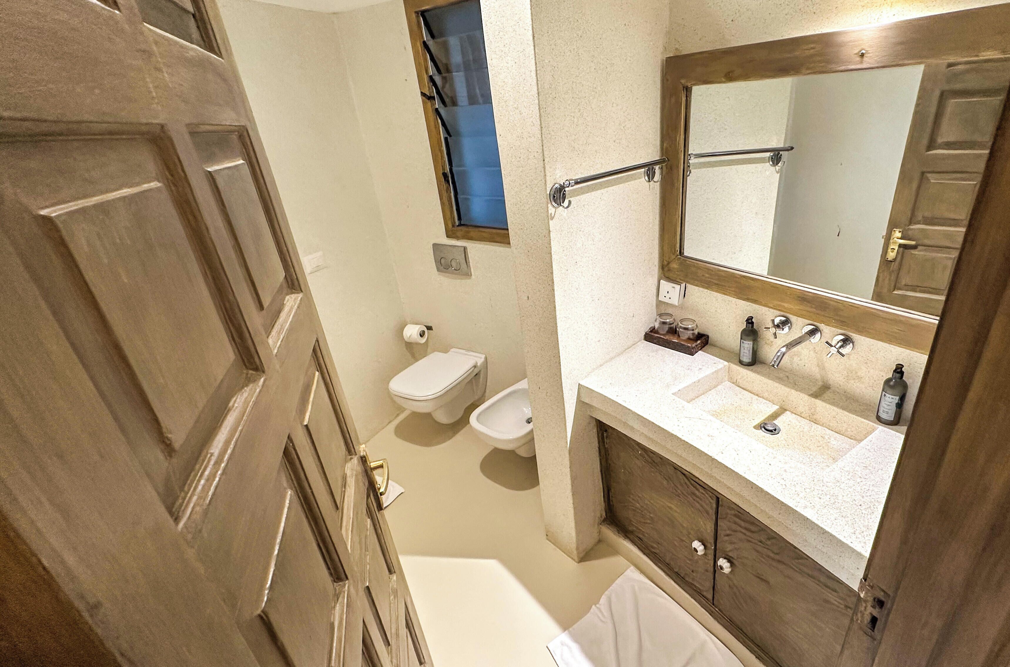 Ein Badezimmer mit Holztür, Toilette, Waschbecken mit Spiegel und Badewanne.
