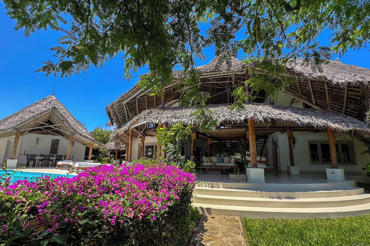 Um resort com edifícios de telhado de palha, piscina e vegetação exuberante.