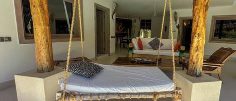 A room with a hanging swing bed, a dining area, and a view of the outdoors.
