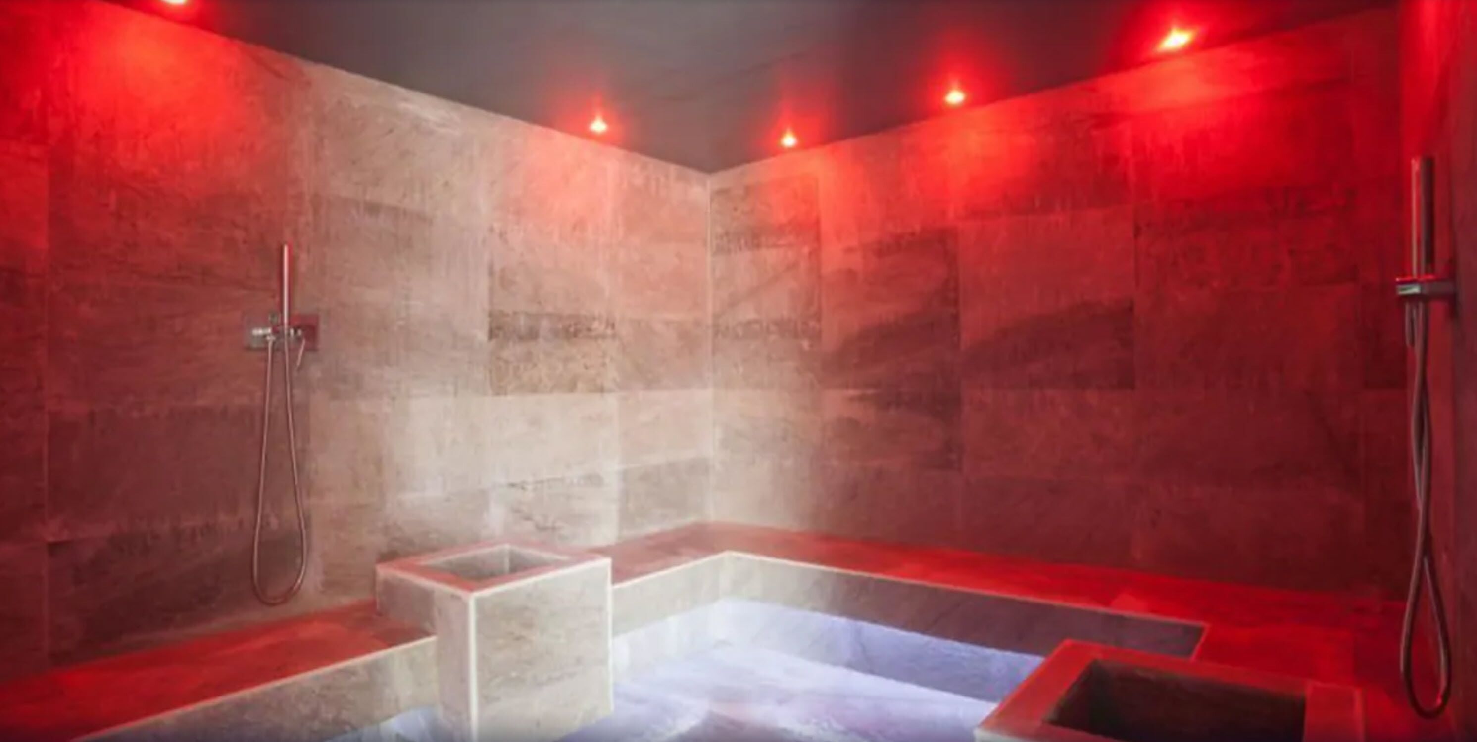 A steam room with a rectangular bench, a shower area, and red lighting.