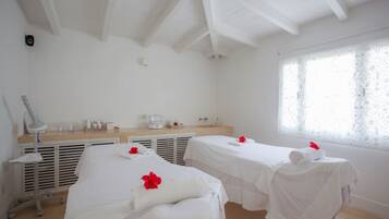 Una stanza spa con due letti, un comò con articoli da toilette e un'ampia finestra con tende di pizzo.