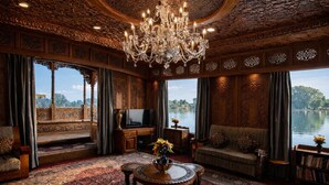 A luxurious room with a large chandelier, ornate wooden paneling, a television, and a view of a lake. - Mascot Houseboats (Srinagar)