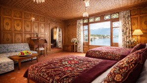 A room with a large bed, a sofa, and a table with fruit. There are windows with curtains and a view of a body of water. - Mascot Houseboats (Srinagar)