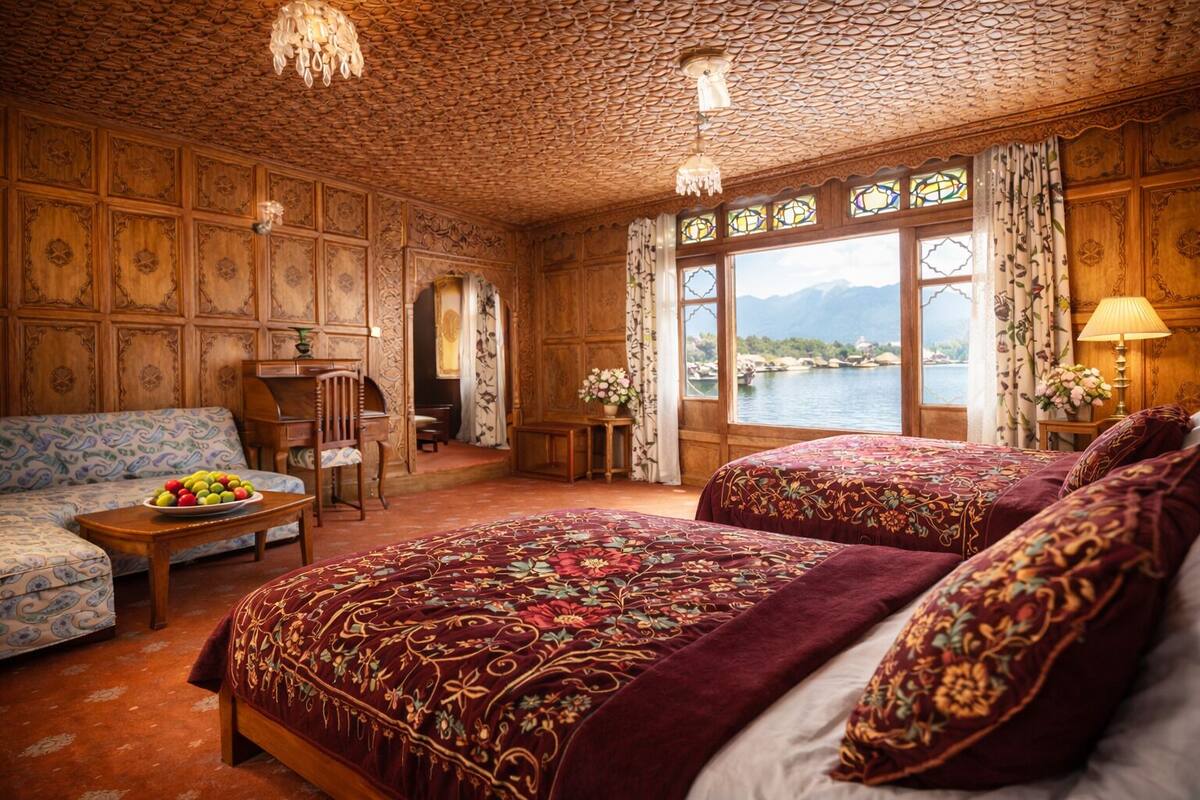 A room with a large bed, a sofa, and a table with fruit. There are windows with curtains and a view of a body of water.