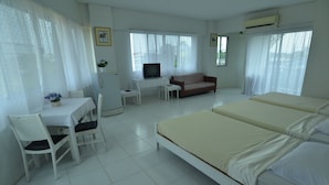 A hotel room with a bed, a desk with a TV, a chair, a sofa, and a window with curtains. - Chomdao Hotel (Rayong)
