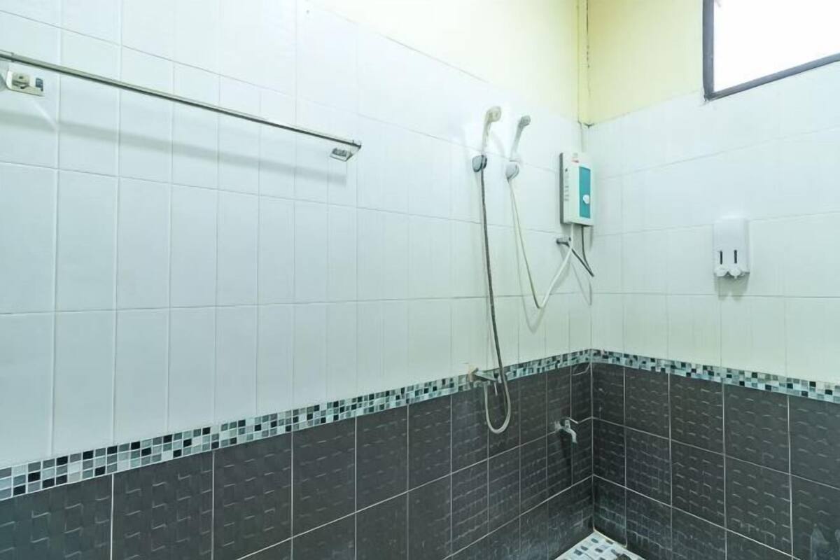 A bathroom with white tiled walls, a black and white tiled floor, a shower with a handheld showerhead, and a wall-mounted faucet.