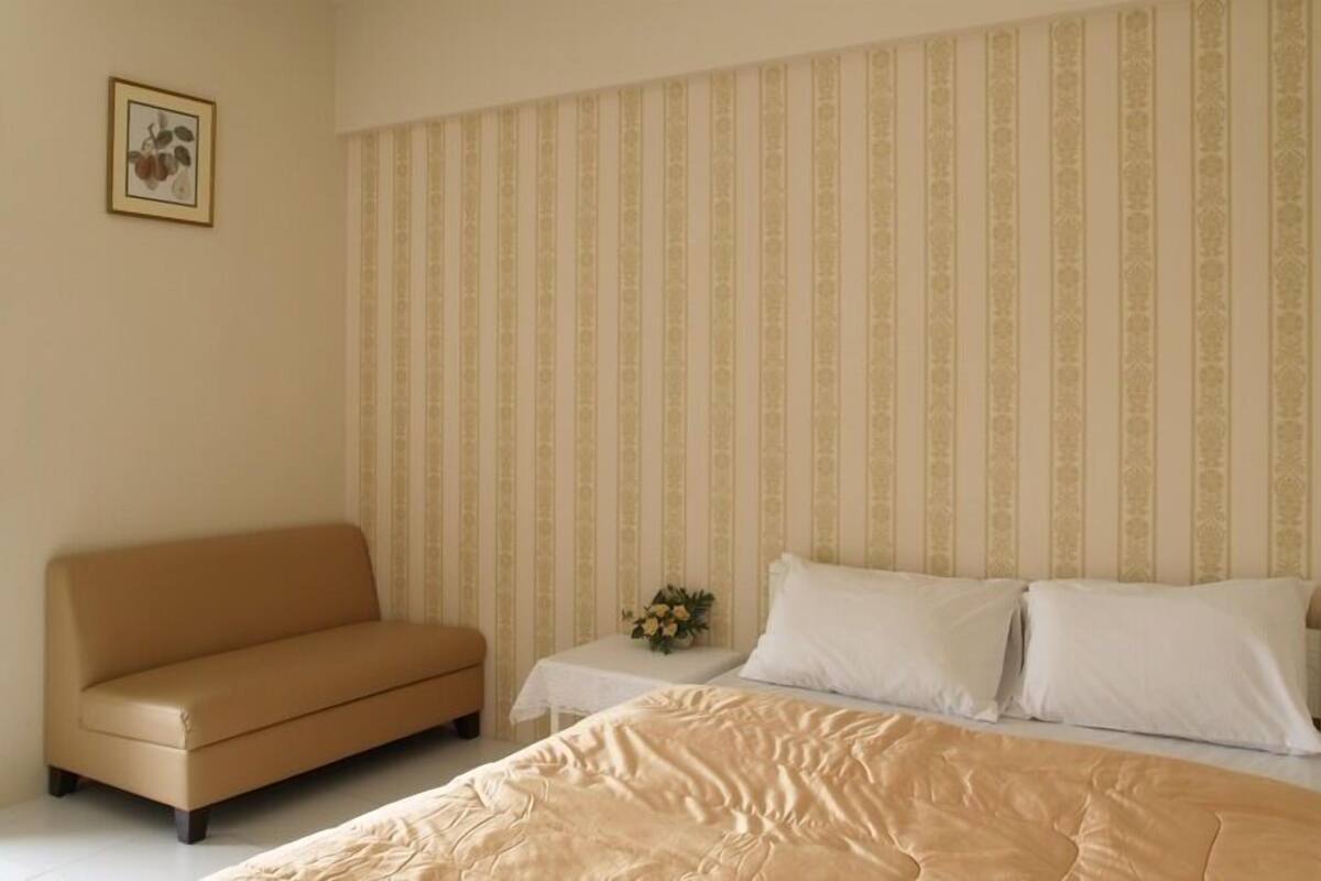 A bedroom with a bed, a sofa, and a nightstand with a vase of flowers.
