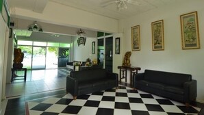A spacious room with a black and white checkered floor, two black sofas, a ceiling fan, and wall-mounted artwork. - Chomdao Hotel (Rayong)