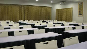 A conference room with rows of tables and chairs, a ceiling with recessed lighting, and curtains on the windows.