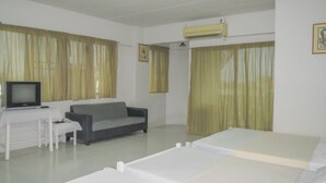 A hotel room with a bed, a sofa, a desk with a television, and curtains. - Chomdao Hotel (Rayong)
