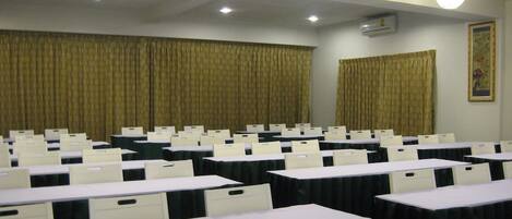 Ein Konferenzraum mit Reihen von Tischen und Stühlen, einer Decke mit eingelassenen Leuchten und einem großen Vorhang an einer Wand.