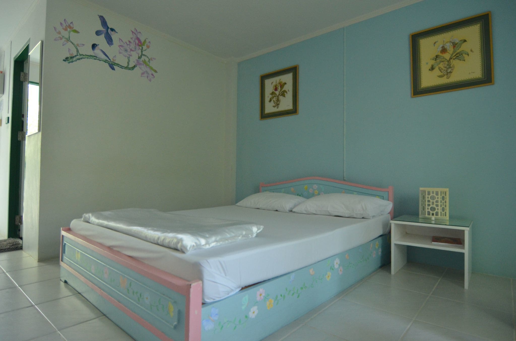 A bedroom with a bed, a nightstand, and two framed pictures on the wall.