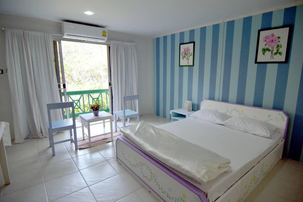 A bedroom with a bed, a chair, a small table, and a window with curtains.