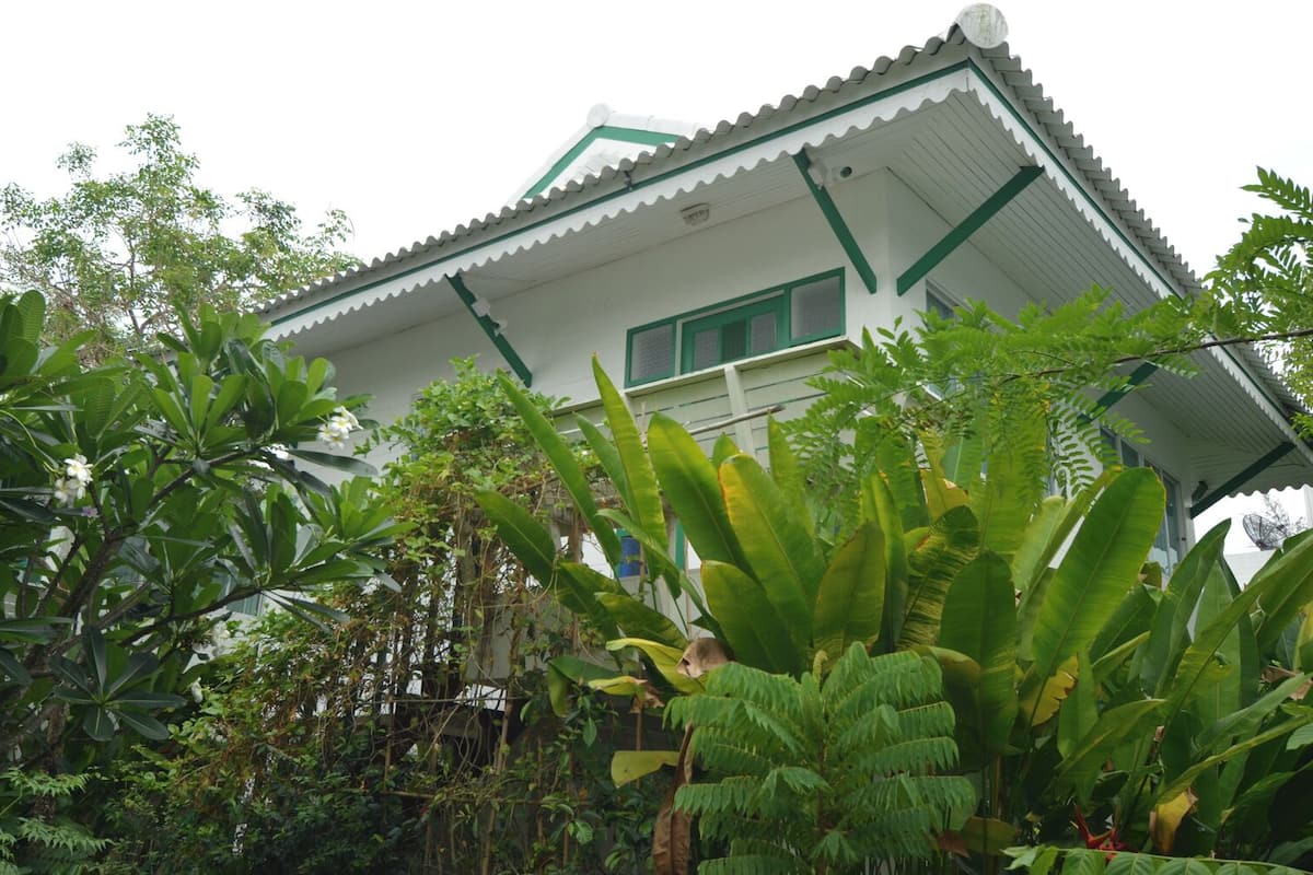 A traditional house with a tiled roof, surrounded by lush greenery and banana plants.