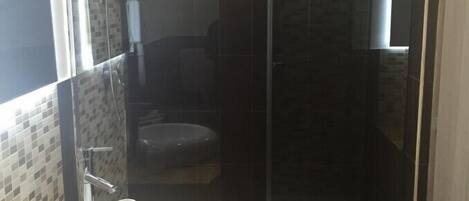 Un baño moderno con cabina de ducha de vidrio, un lavamanos blanco y un espejo.