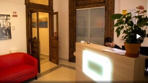 Zona de recepción con mostrador de madera, un sofá rojo y una planta en maceta.