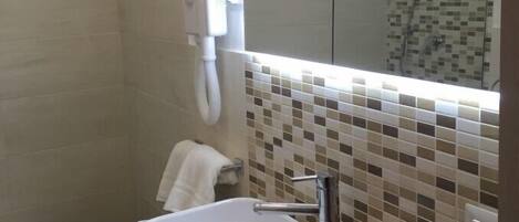 Une salle de bain moderne avec un lavabo blanc, une douche en verre et un mur recouvert de carreaux.