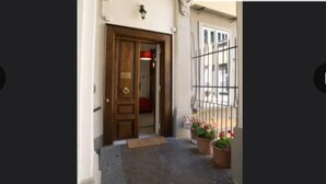 Una entrada estrecha con una puerta de madera, un pequeño escalón para entrar y un portón con plantas en macetas.