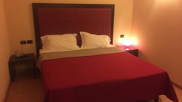 A standard hotel room with a single bed, a nightstand, a bedside table, and a wall-mounted lamp.