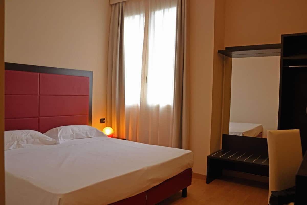 Una habitación de hotel con una cama grande, una mesita de noche con lámpara, una silla y un armario.