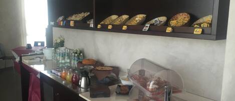 Una barra de desayuno con diversos alimentos, entre ellos bollería y bebidas, además de una máquina de café.