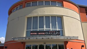 Un hotel amb una façana corba, finestres grans i un rètol que diu "HOTEL - MOTEL GALAXY".