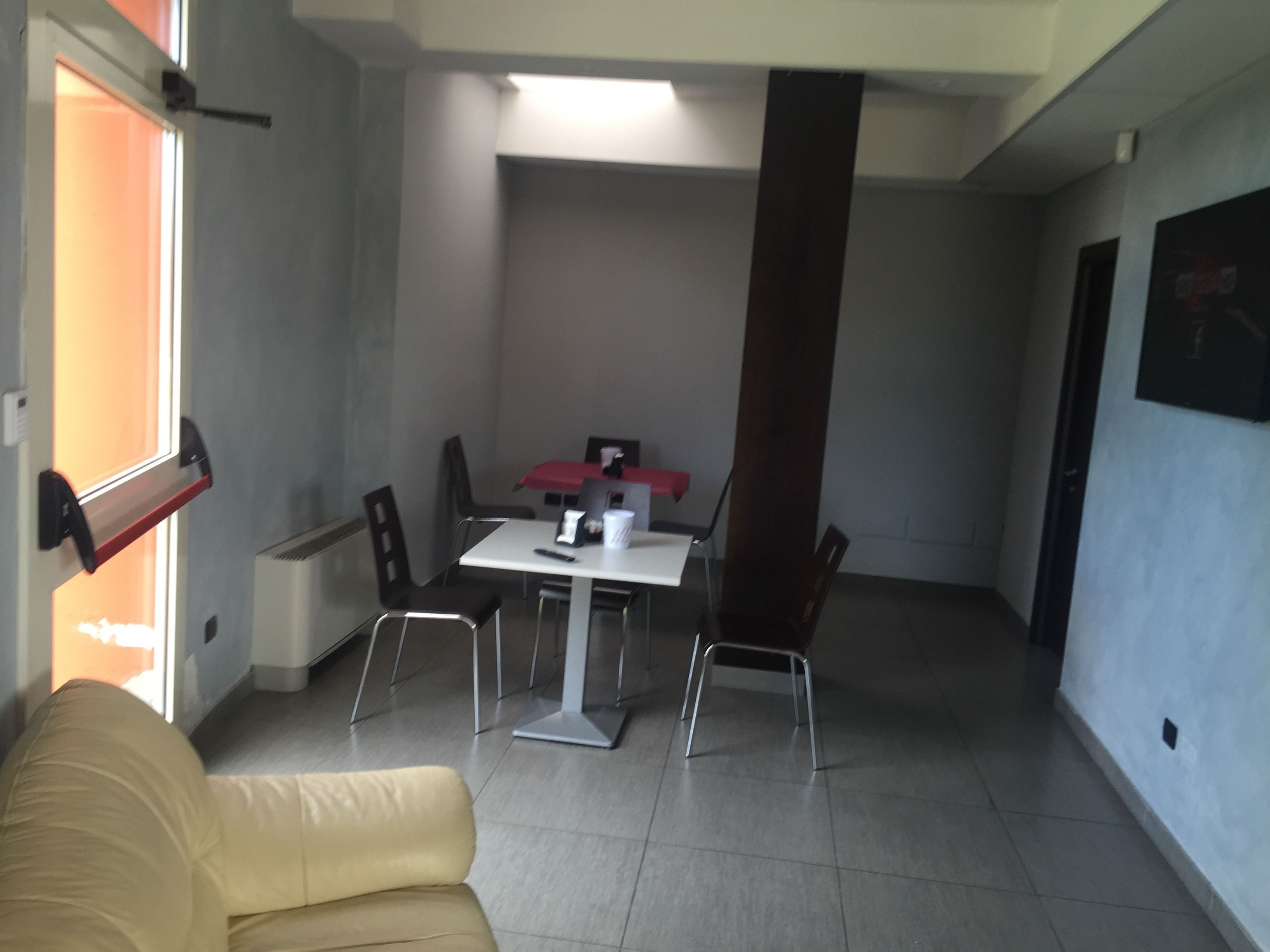 Una habitación pequeña y moderna con un sofá individual, una mesa de comedor con cuatro sillas y una ventana con vistas al exterior.